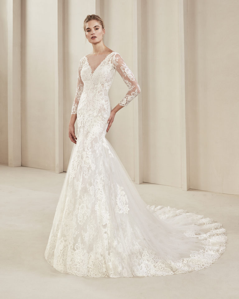 Mermaid-style lace wedding dress. With V-neckline, low back and long sleeves. Available in natural. 2019 ALMA_NOVIA Collection.