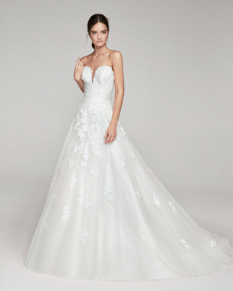 Romantic wedding dress in tulle and beaded lace. With deep-plunge neckline. Skirt with lace appliqués. Available in pink and natural. 2019 ALMA_NOVIA Collection.
