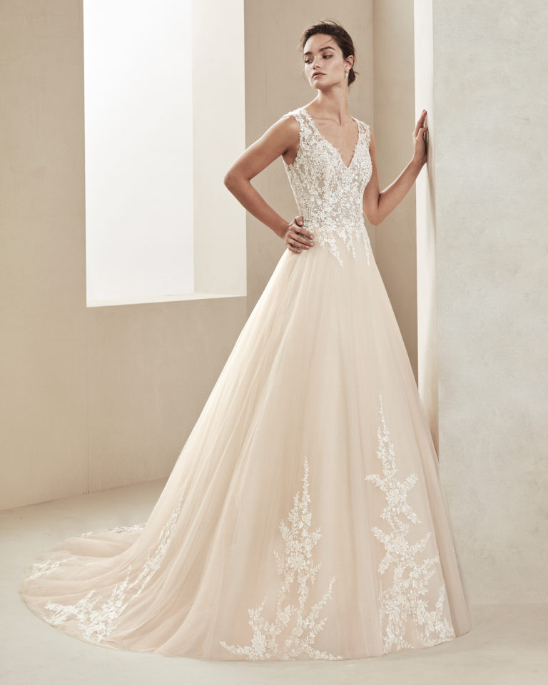 Romantic tulle and lace wedding dress. With V-neckline and tulle and lace back. Skirt with lace appliqués. Available in amber and natural. 2019 ALMA_NOVIA Collection.