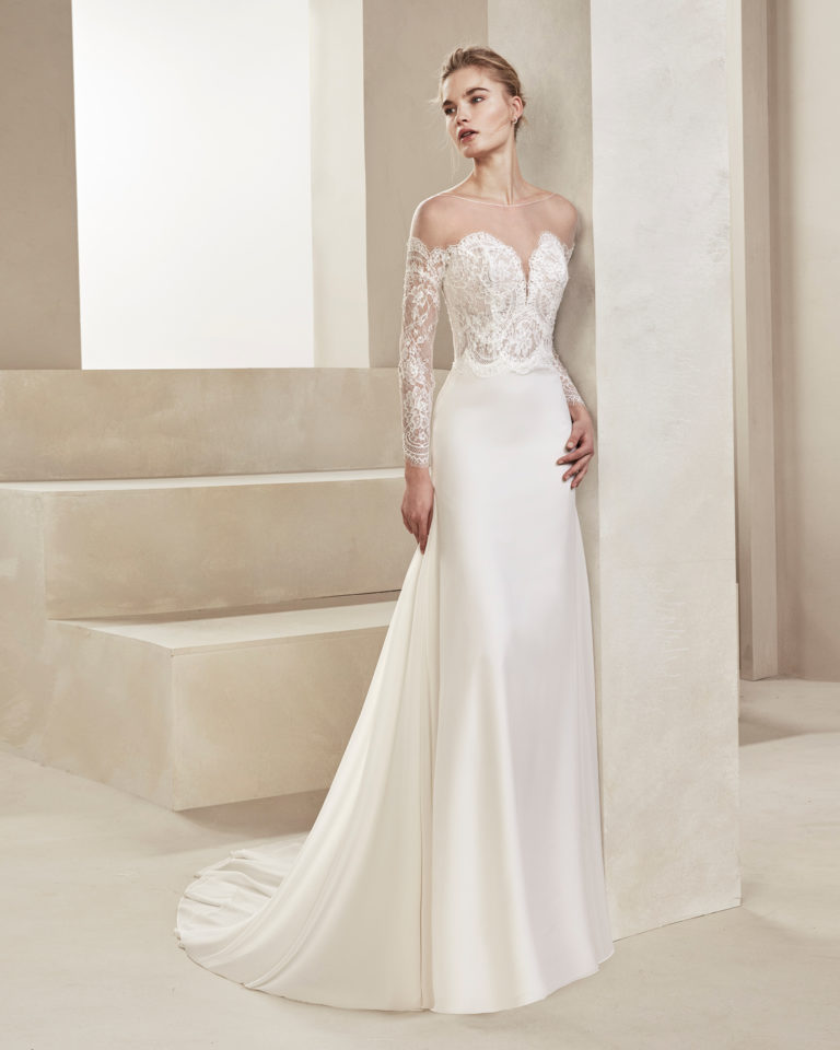 Sheath-style wedding dress in crepe Georgette and beaded lace. With sweetheart neckline and long lace sleeves. Available in natural. 2019 ALMA_NOVIA Collection.