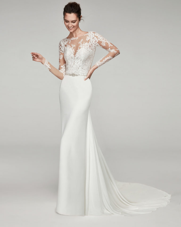 Sheath-style wedding dress in chiffon and lace. With illusion neckline and long lace sleeves. With beaded brooch. Available in natural. 2019 ALMANOVIA Collection.