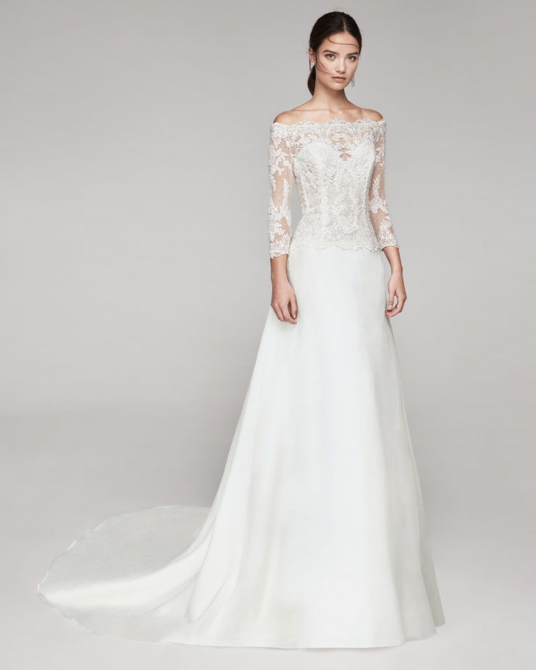 Elegant wedding dress in organza and beaded lace. With off-the-shoulder neckline and three-quarter lace sleeves. Available in natural. 2019 ALMANOVIA Collection.