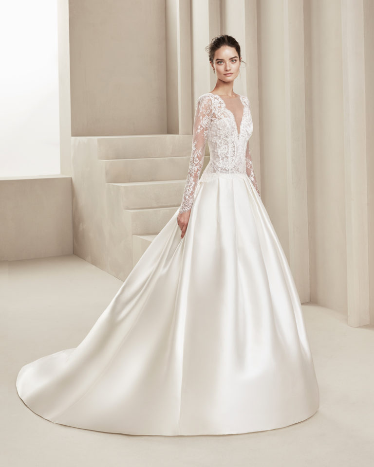 Classic wedding dress in tammy and beaded lace. With deep-plunge neckline, low back and long lace sleeves. With train. Available in natural. 2019 ALMANOVIA Collection.