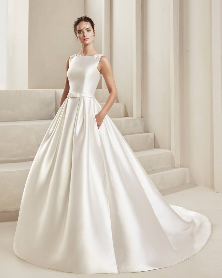 Classic tammy wedding dress. With low V-back and beading. With bow in front at the waist. Available in natural. 2019 ALMA_NOVIA Collection.