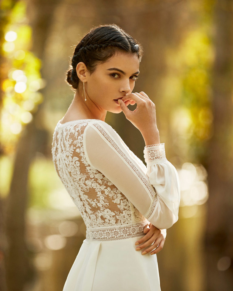 Boho-style crepe and lace wedding dress with V-neckline and back with sheer inserts and long bloused sleeves. 2020 ALMA_NOVIA Collection.