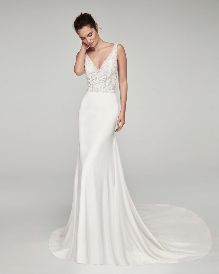 Vestido de novia corte recto en georgette, encaje y pedrería. Con escote V y espalda en V. Disponible en color natural. Colección ALMANOVIA 2020.
