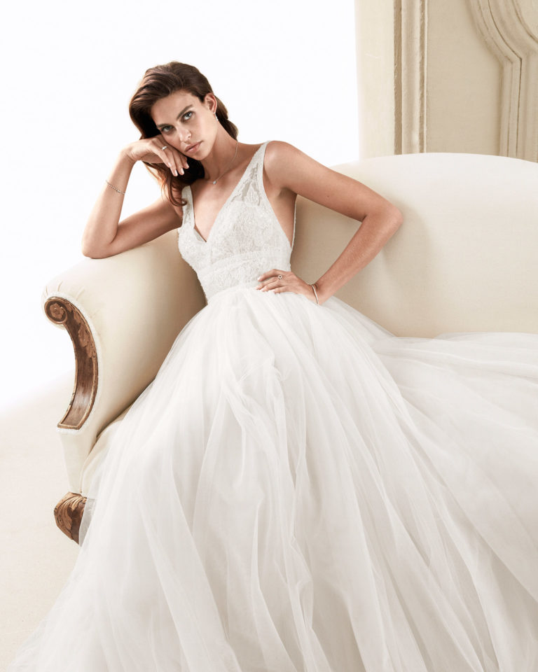 Vestido de novia romántico de tul suave, encaje y pedrería. Con escote V, espalda escotada con línea de pedrería. Disponible en color natural/nude y natural. Colección ALMANOVIA 2020.