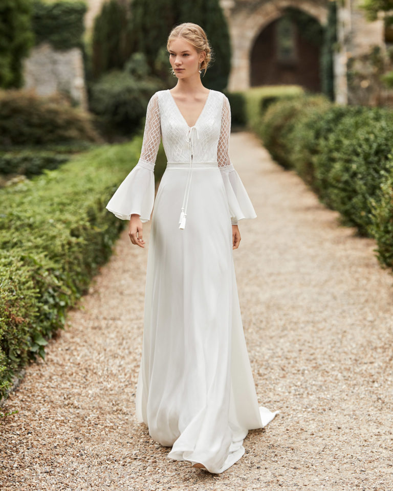 Wedding dress in crepe. V-neckline in lace, braid bow, long flared sleeves in lace and chiffon, lace belt and open teardrop back in lace. 2021 ALMANOVIA Collection.