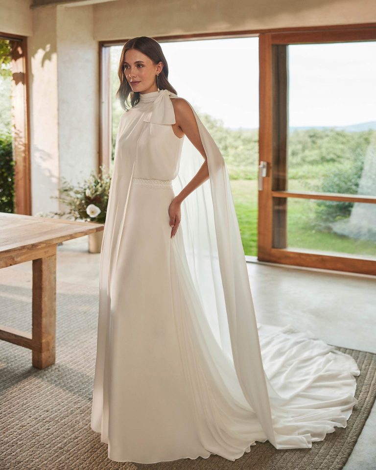  Long bridal dress, two-piece and straight cut. Crafted in georgette with a halter neckline, closed back, and cape. ALMA_NOVIA.