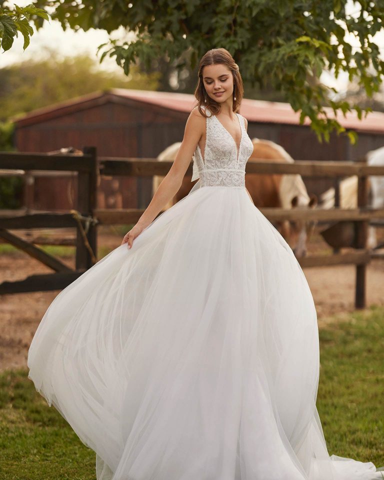 Long bridal dress with a straight cut. Crafted in tulle and lace with a V-neckline, straps, and back with tulle bow. ALMA_NOVIA.
