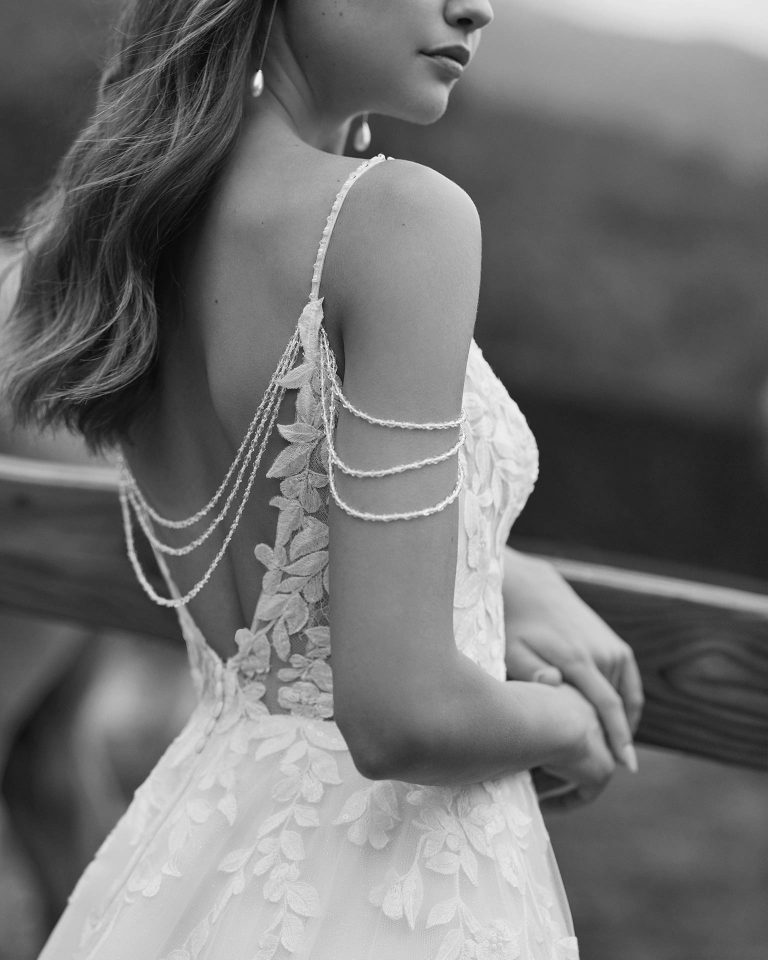 Long bridal dress with an A-line cut. Crafted in glitter tulle and lace with an illusion neckline, dropped straps, and open back. ALMA_NOVIA.