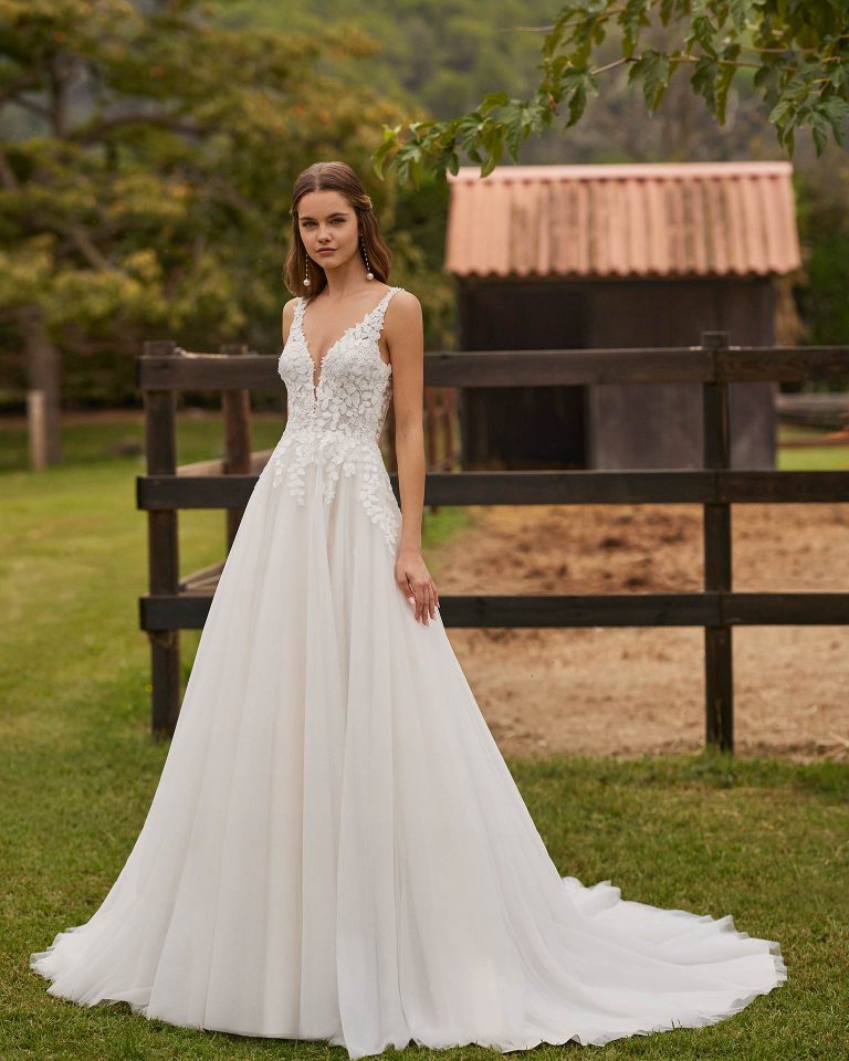 Long bridal dress with an A-line cut. Crafted in glitter tulle and lace with a deep neckline, straps, and open back. ALMA_NOVIA.