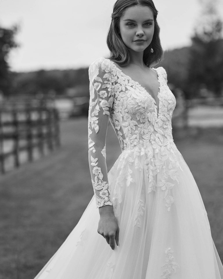Long bridal dress with an A-line cut. Crafted in tulle and lace with a V-neckline, long sleeves, and open back. ALMA_NOVIA.