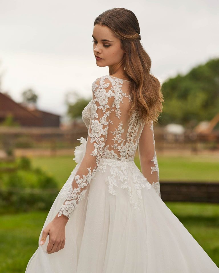 Long bridal dress with an A-line cut. Crafted in tulle and lace with floral embellishments, V-neckline, detachable sleeves, and tattoo back. ALMA_NOVIA.