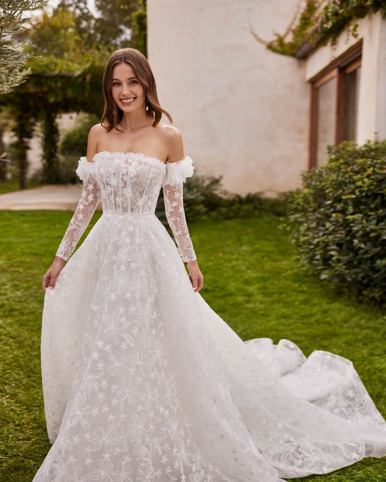 Long bridal dress with an A-line cut. Crafted in lace with a strapless neckline, lace sleeves, and corset back. ALMA_NOVIA.