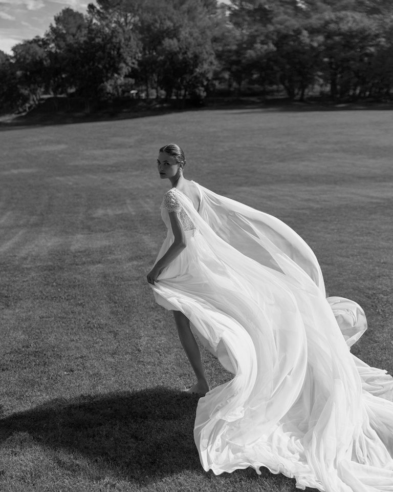 Vestido de novia de dos piezas en muss, silueta recta con escote pico, manga corta con encaje, cuerpo plisado con encaje, falda con abertura delantera, capa incluida, cierre cremallera. ALMA_NOVIA.