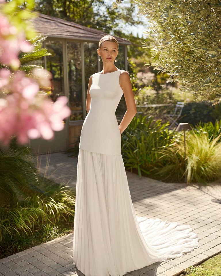 Vestido de novia de silueta recta con escote barco y espalda cuadrada. Cuerpo en crepé liso y falda plisada extraíble. Cierre con cremallera. ALMA_NOVIA.