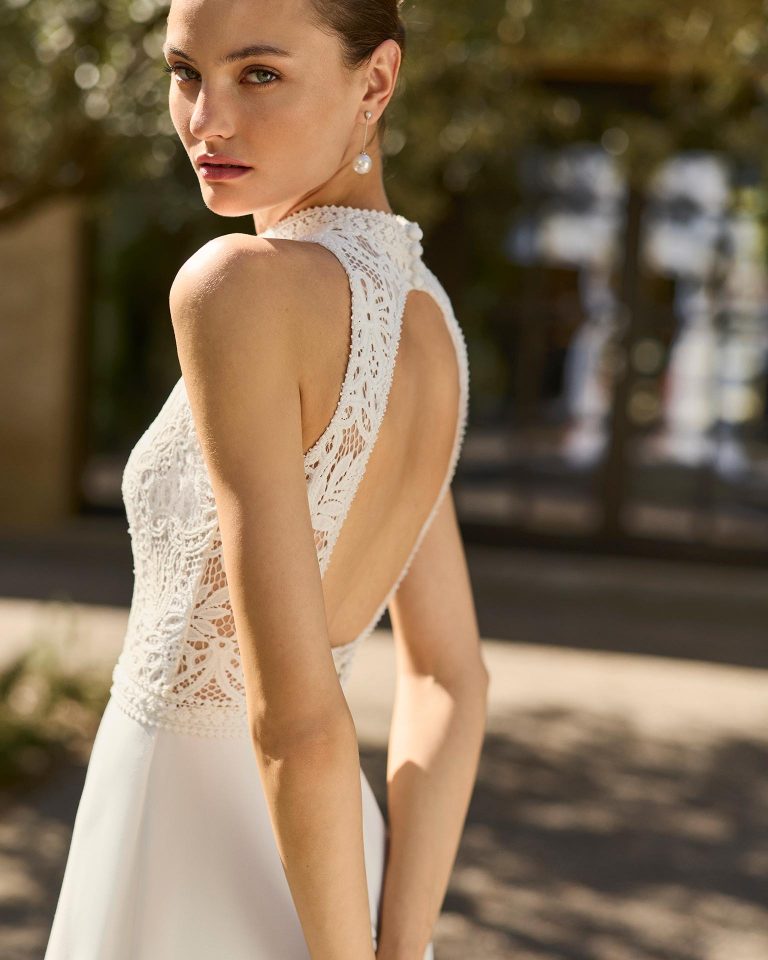 Vestido de novia línea A con escote halter, cuerpo de encaje, espalda abierta, falda de crepé elástico lisa con abertura delantera. ALMA_NOVIA.