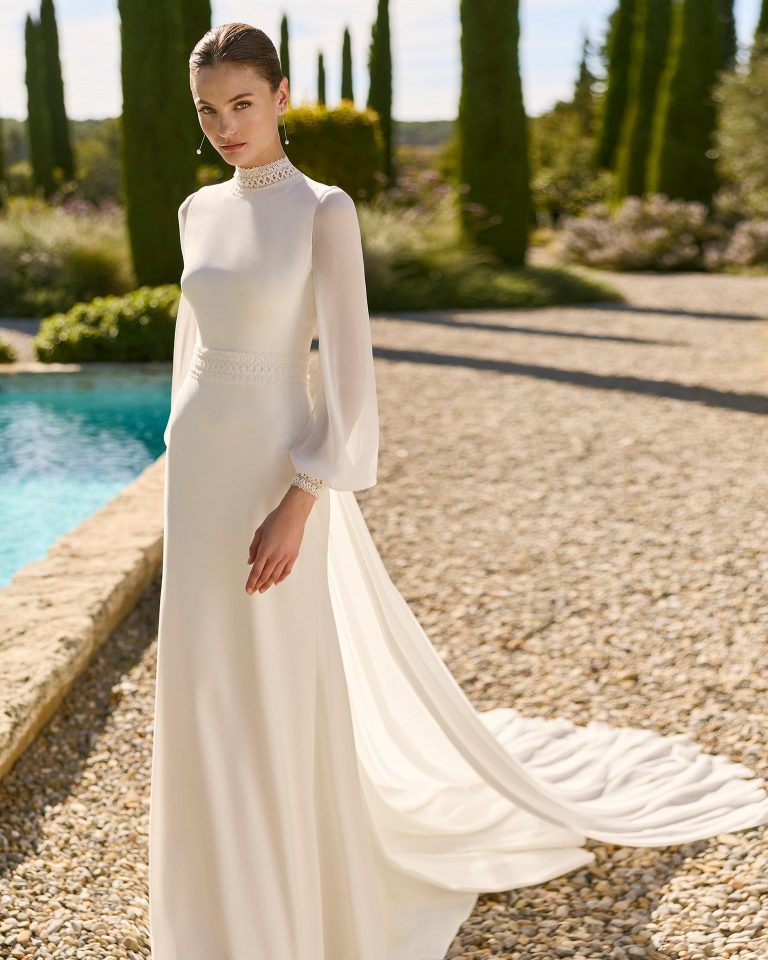 Vestido de novia de dos piezas en crepé elástico con silueta recta, cuello cisne, manga larga poeta extraíble, pedrería en el cuerpo, espalda con abertura, incluye cola lisa. ALMA_NOVIA.